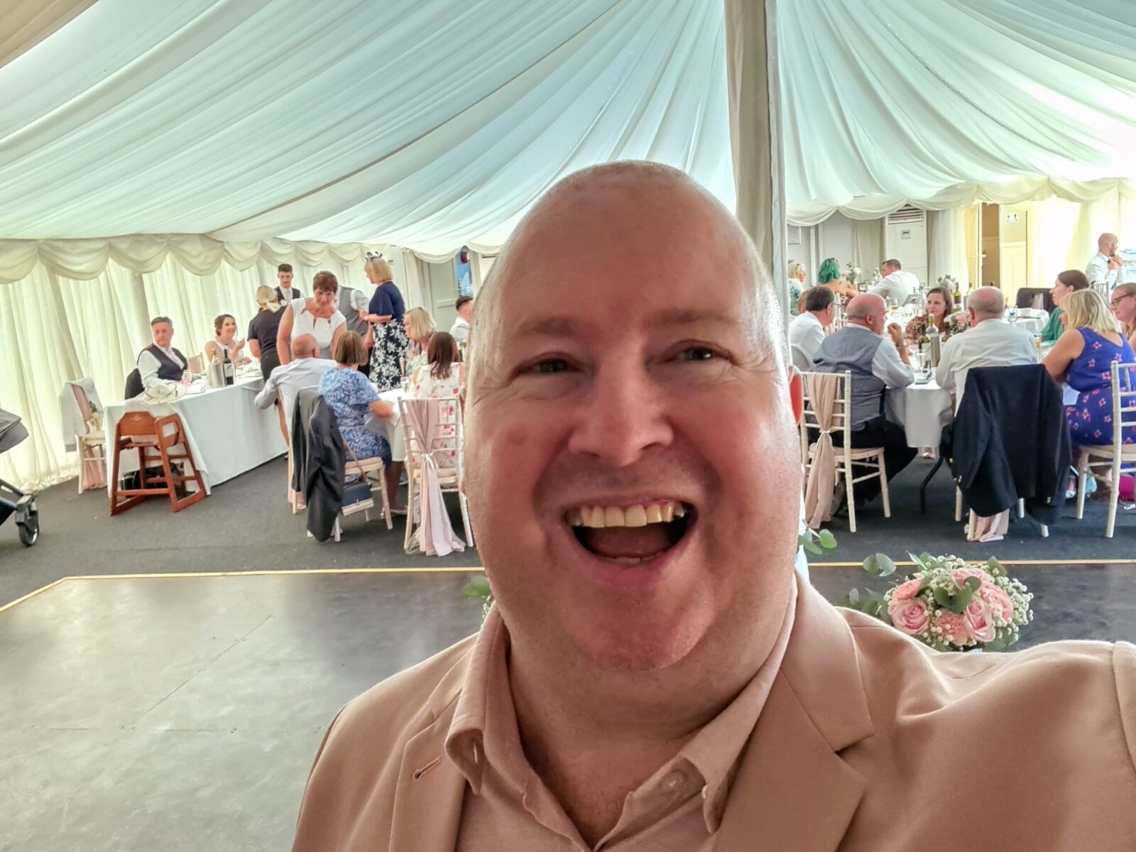 Smiling wedding host/MC in pink suit with seated wedding crowd in background